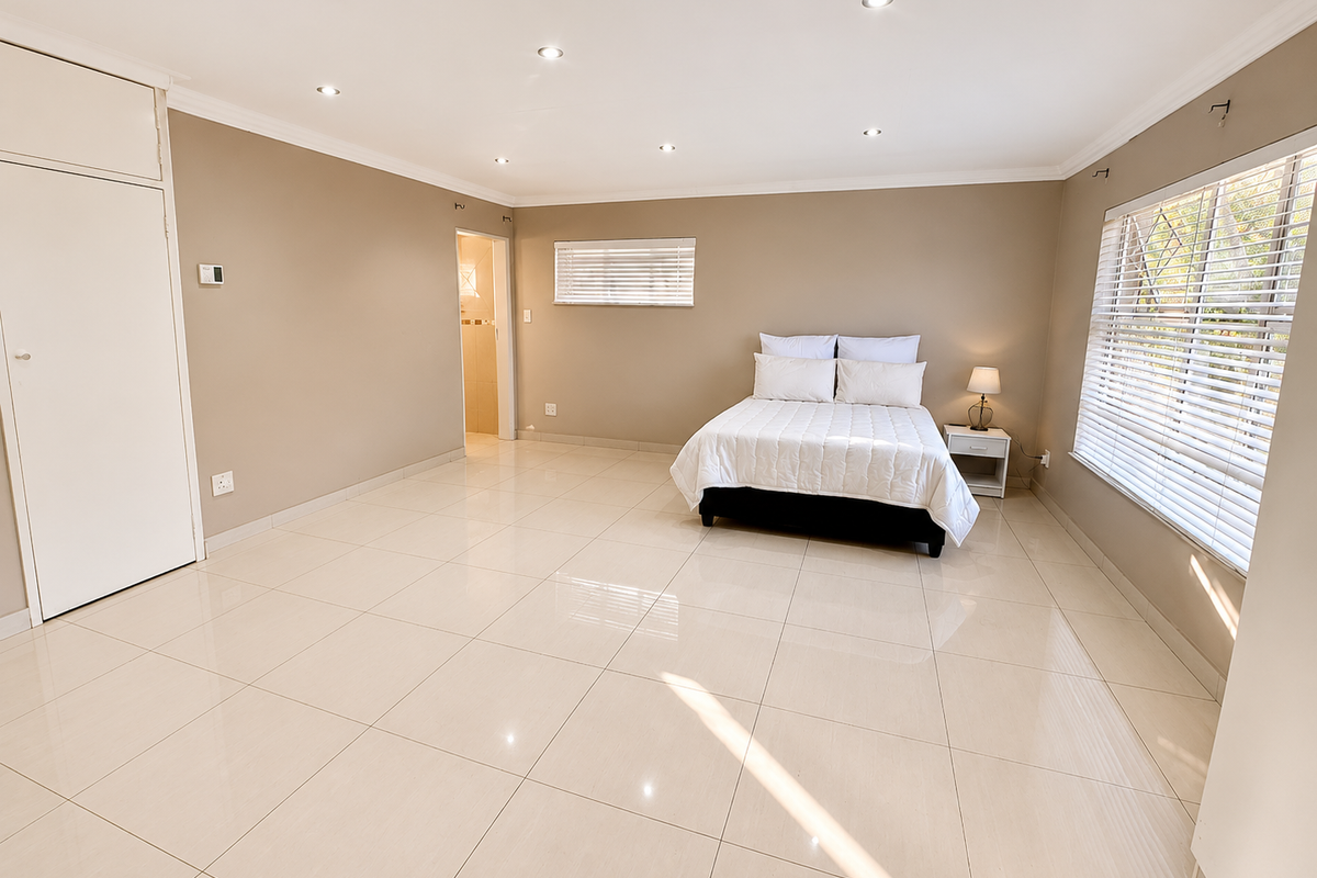 Spacious bedroom featuring neutral tiled flooring, built-in cupboards, recessed downlighting, and large windows with venetian blinds, offering a clean and bright living space.