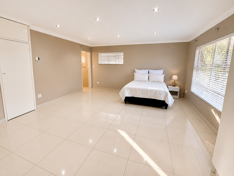 Spacious bedroom featuring neutral tiled flooring, built-in cupboards, recessed downlighting, and large windows with venetian blinds, offering a clean and bright living space.