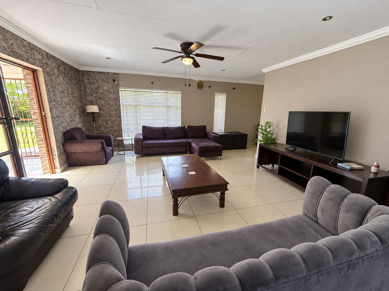 Spacious living room featuring large format floor tiles, a textured feature wall, recessed lighting, and a ceiling fan with direct access to the patio.