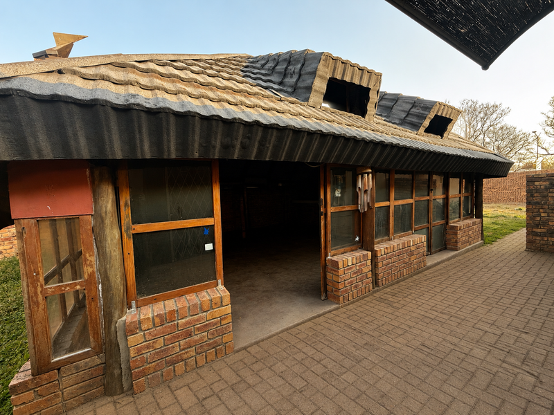 A rustic outdoor patio area featuring a tiled roof with dormer windows, brick base construction, and paved flooring, offering a potential covered entertainment space.