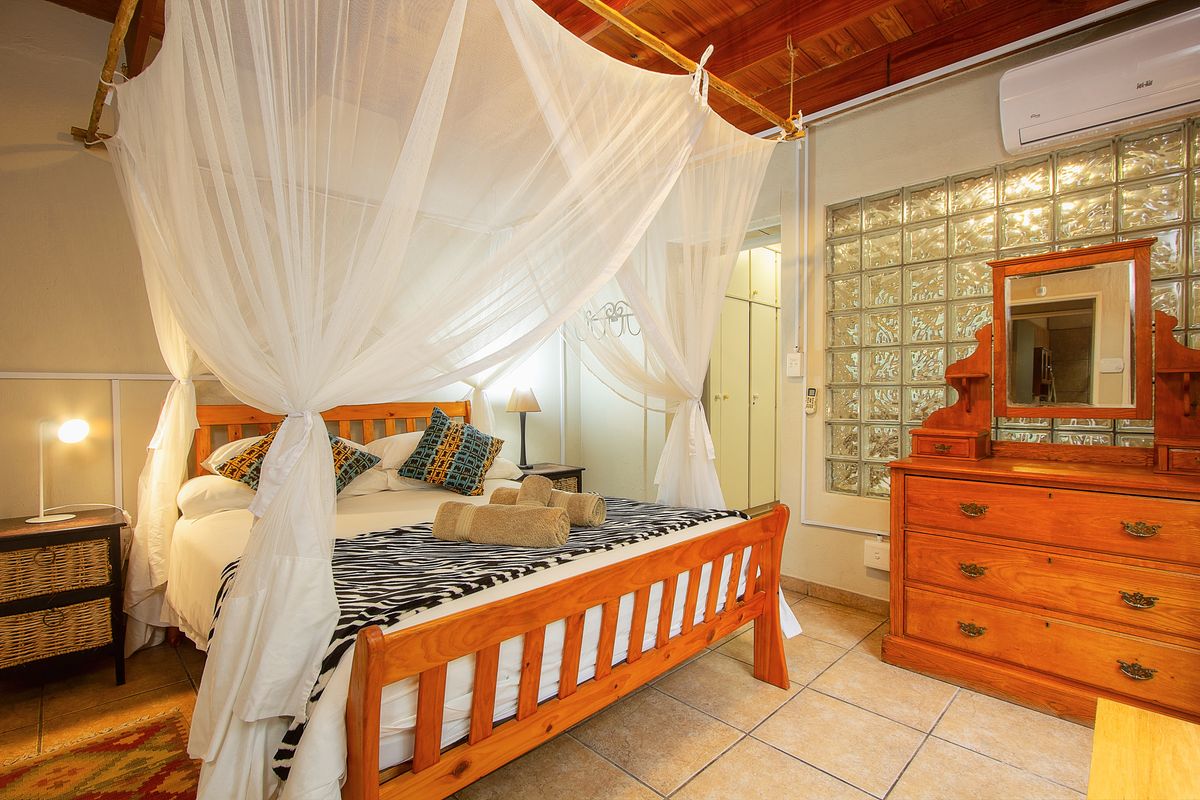A bedroom featuring a timber ceiling, tiled flooring, a glass block feature wall, and a wall-mounted split system air conditioner.
