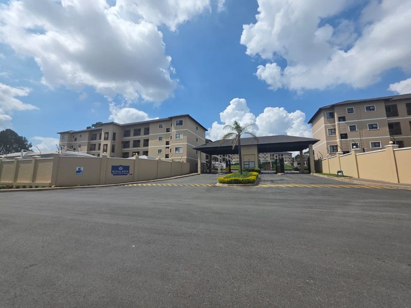 The main entrance to the Royal Reef apartment complex, featuring a secure gatehouse, perimeter walling, and well-maintained multi-story residential buildings.