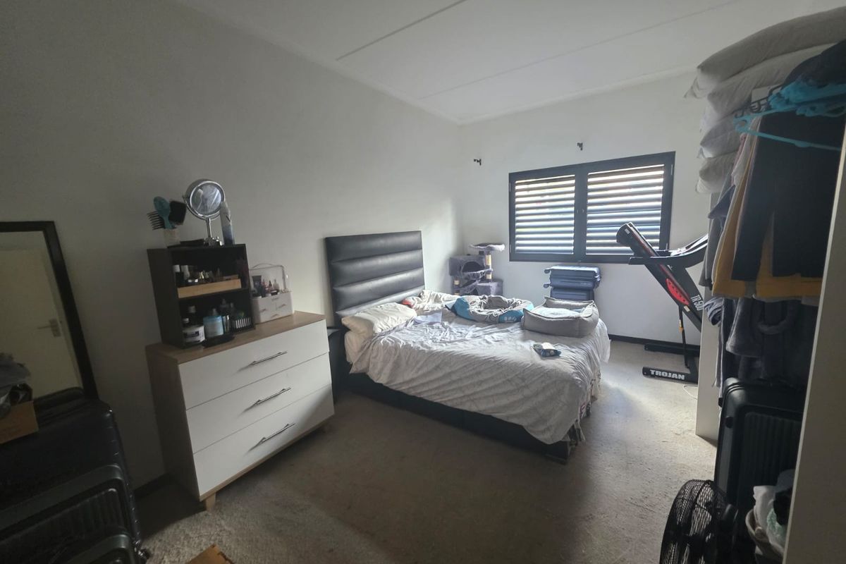 A standard bedroom featuring neutral walls, carpeted flooring, and a window fitted with integrated security shutters.