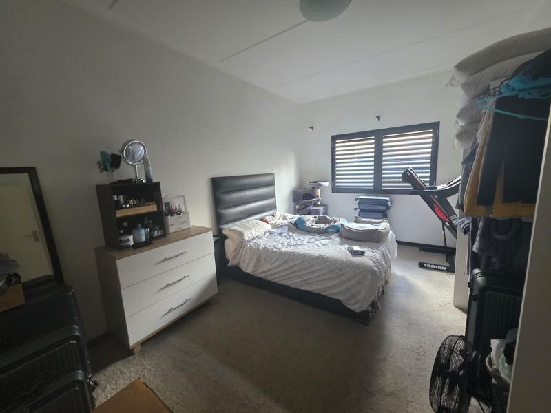 A standard bedroom featuring neutral walls, carpeted flooring, and a window fitted with integrated security shutters.