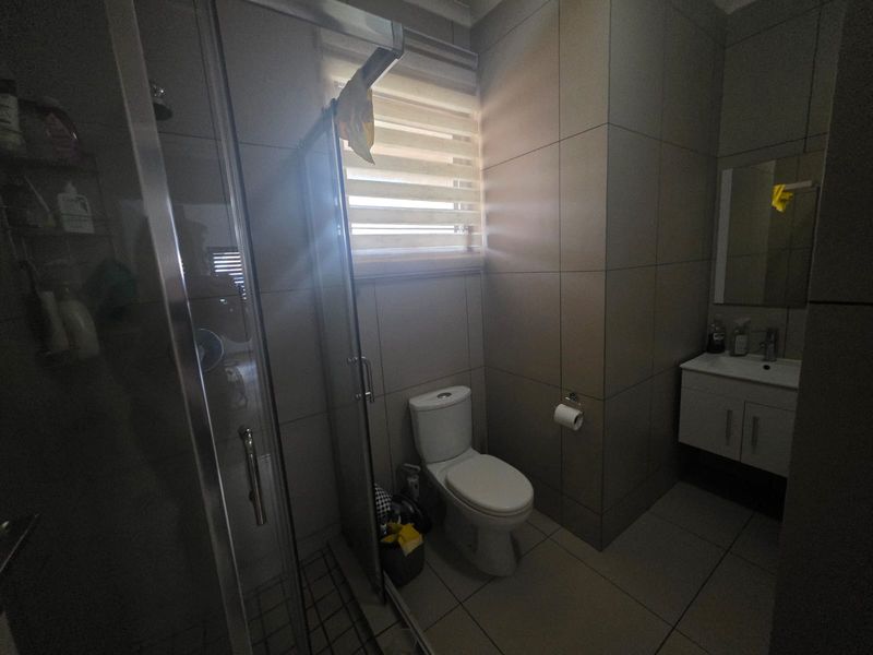 A modern bathroom featuring a glass shower enclosure, wall-mounted vanity, and neutral floor-to-ceiling tiling with a functional roller blind.