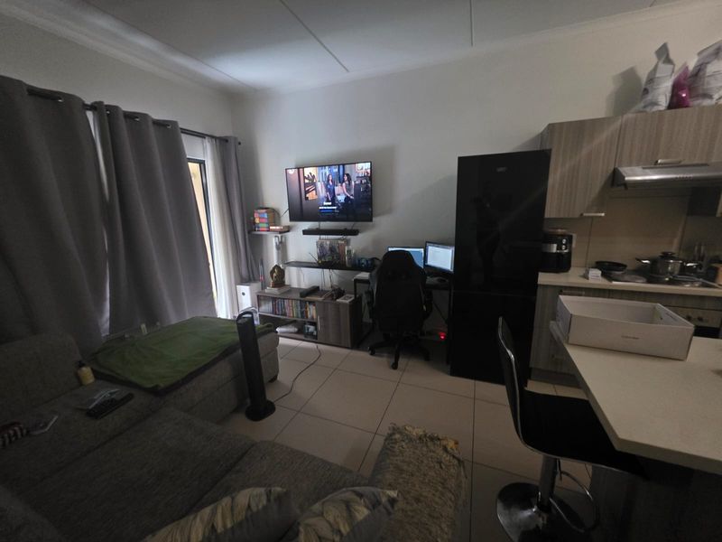 Open-plan living area featuring a compact kitchen with built-in cabinetry and tiled flooring, seamlessly connected to the lounge space with access to a balcony.