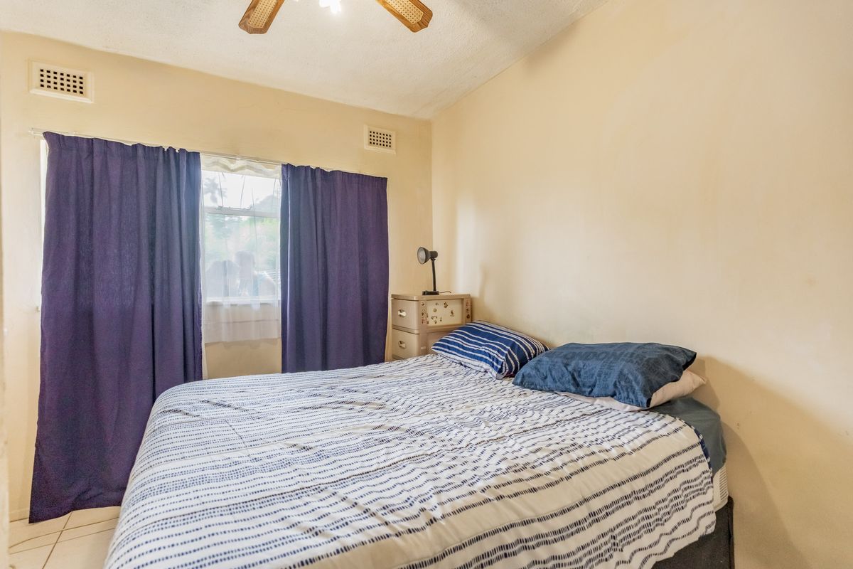 A bedroom featuring tiled flooring, ceiling fan, and ventilation grilles. The room requires cosmetic updates to improve its overall condition and appeal.