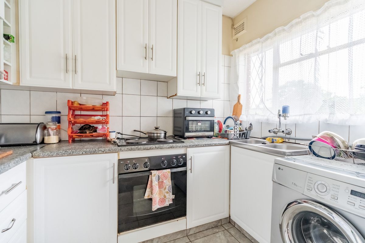 A functional kitchen featuring white cabinetry, laminate countertops, a built-in oven with hob, and a stainless steel sink with tiled backsplash.