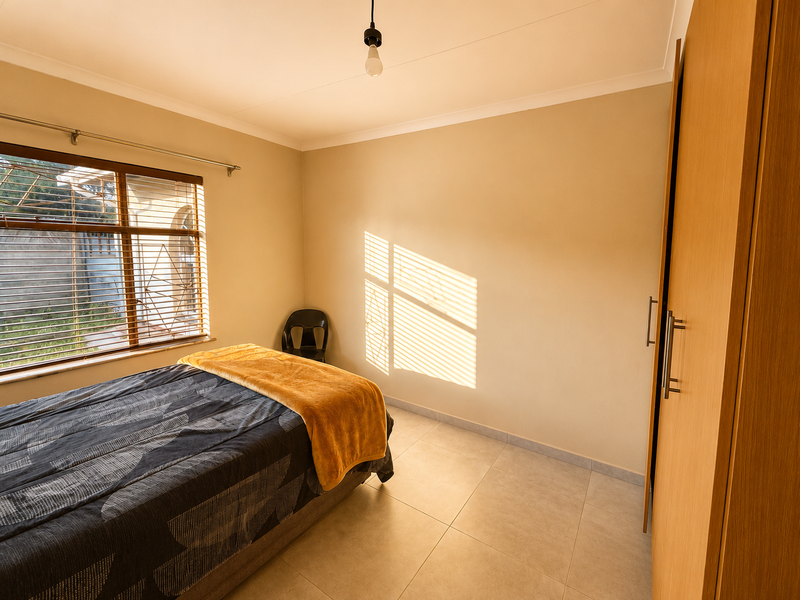 A bedroom featuring tiled flooring, a built-in wardrobe, and natural light filtering through venetian blinds.