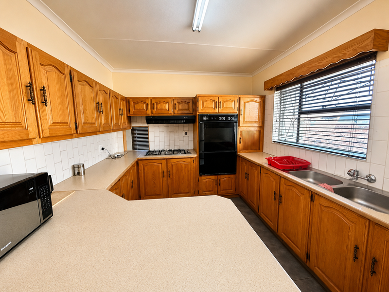 A functional kitchen featuring traditional wooden cabinetry, laminate countertops, a built-in oven, gas hob, and a double basin sink with tiled backsplash.
