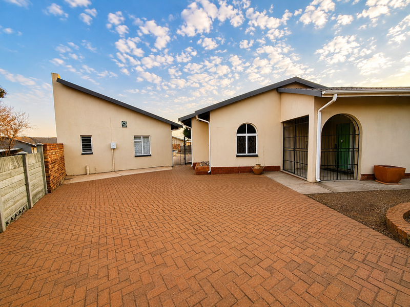 Front exterior view of the property featuring a spacious paved driveway, secure gated entrance, and well-maintained building facade with arched architectural details.