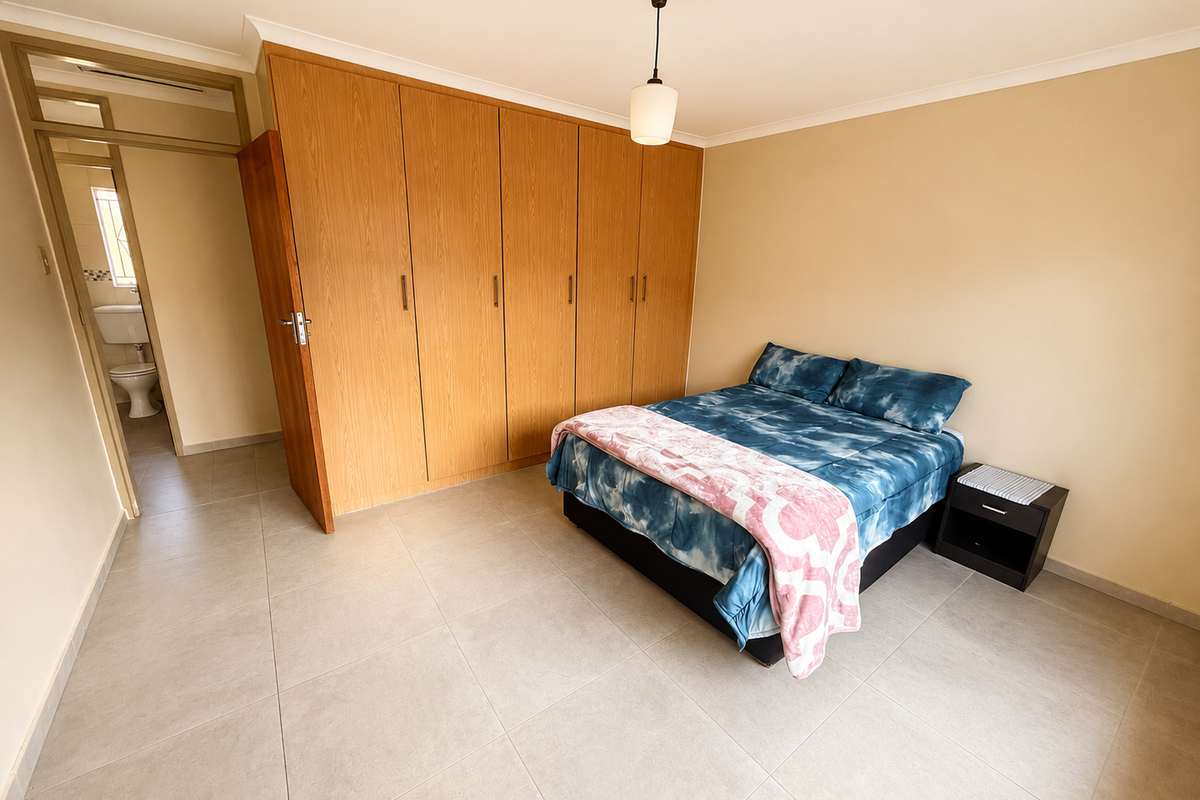 Spacious bedroom featuring neutral tiled flooring, extensive built-in wooden cupboards, and convenient access to an en-suite bathroom.