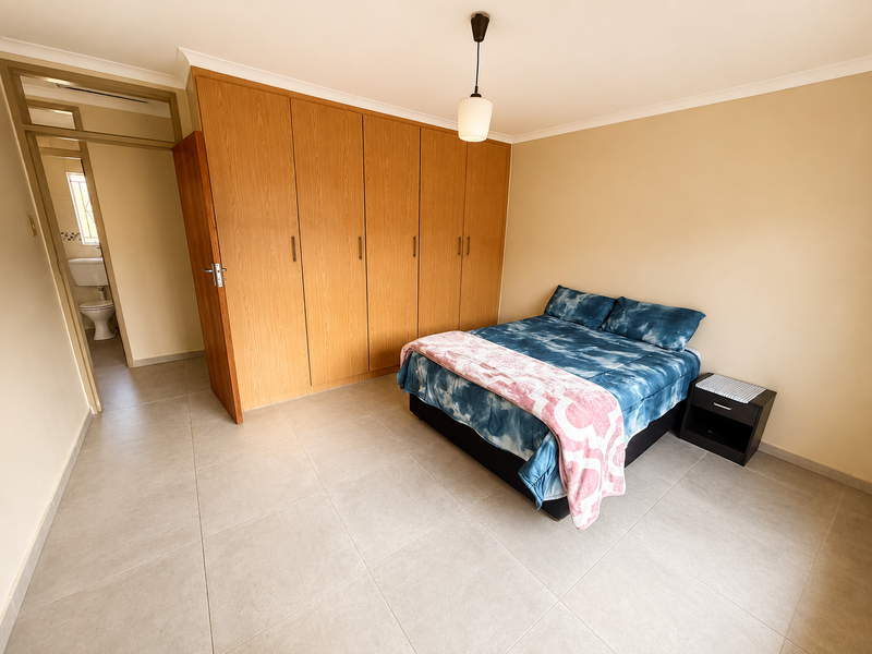 Spacious bedroom featuring neutral tiled flooring, extensive built-in wooden cupboards, and convenient access to an en-suite bathroom.