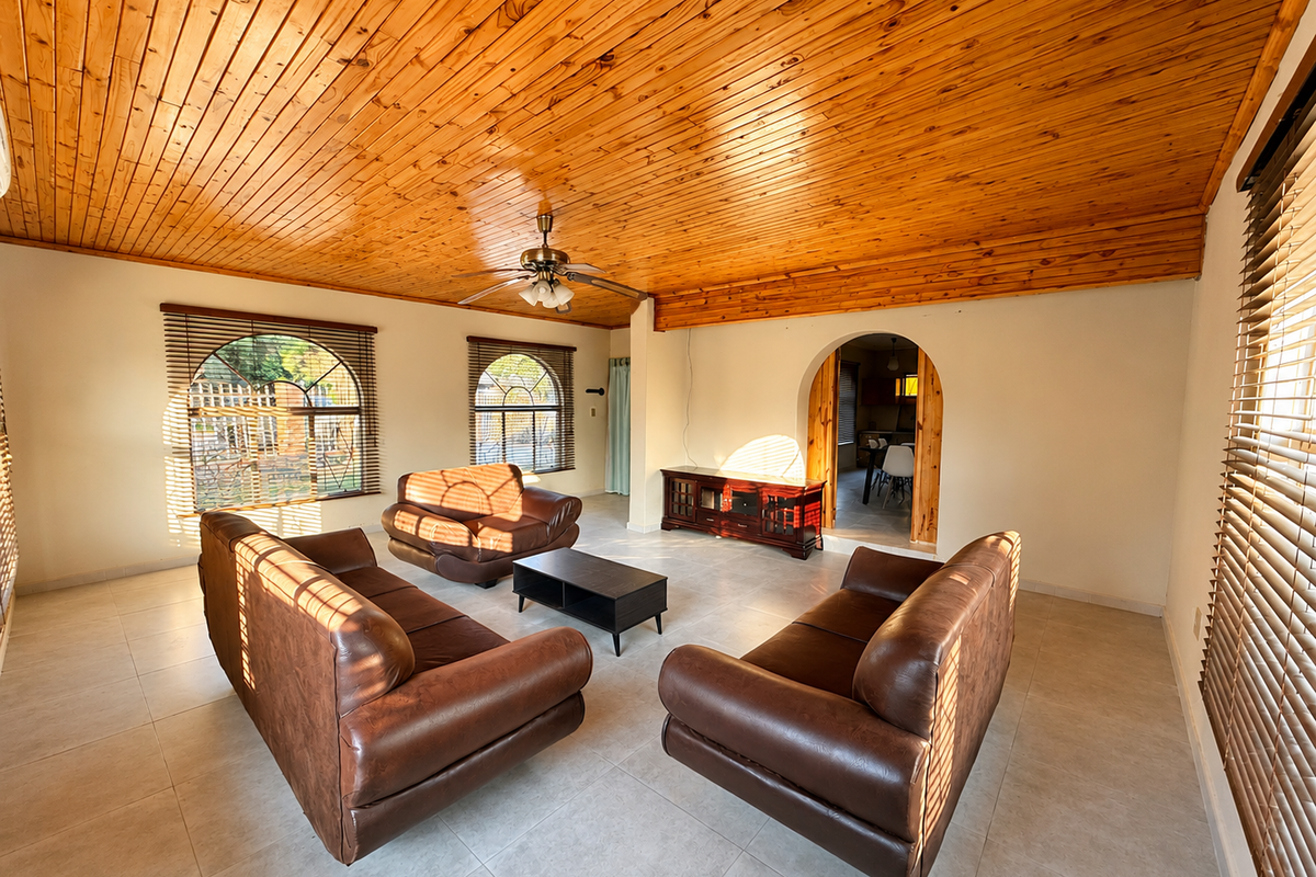 Spacious living room featuring a warm timber tongue and groove ceiling, tiled flooring, and arched windows with venetian blinds, leading to an adjacent room.