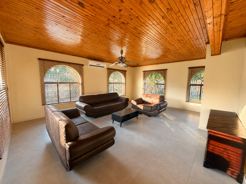 Spacious living room featuring a warm timber tongue and groove ceiling, arched windows with venetian blinds, tiled flooring, and a split-system air conditioner.