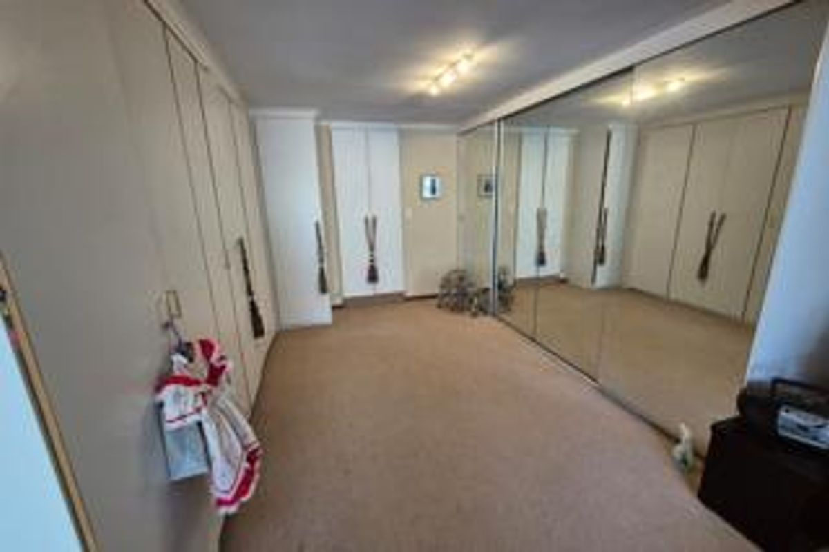 Spacious bedroom featuring extensive built-in cabinetry and large mirrored sliding wardrobe doors, providing ample storage and a bright, open feel.