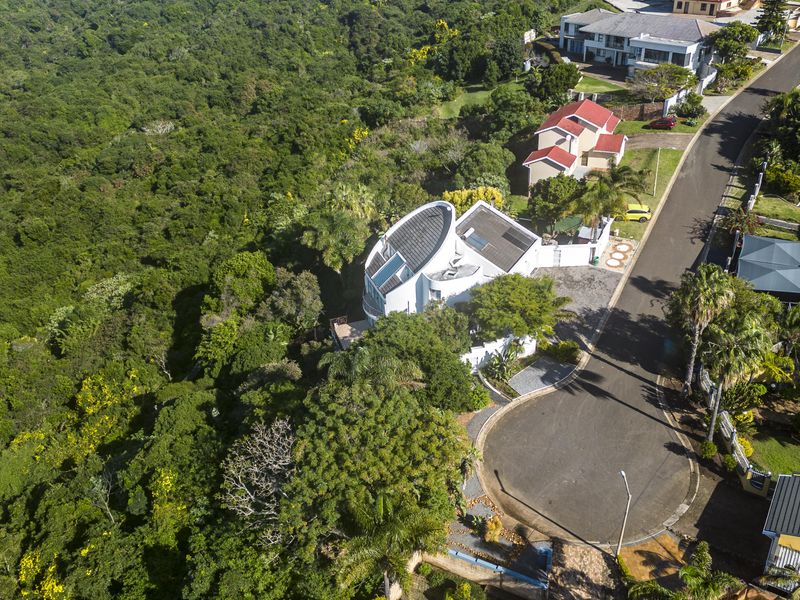Aerial view of a modern residential property situated in a quiet cul-de-sac, featuring solar panels and extensive surrounding natural greenery.