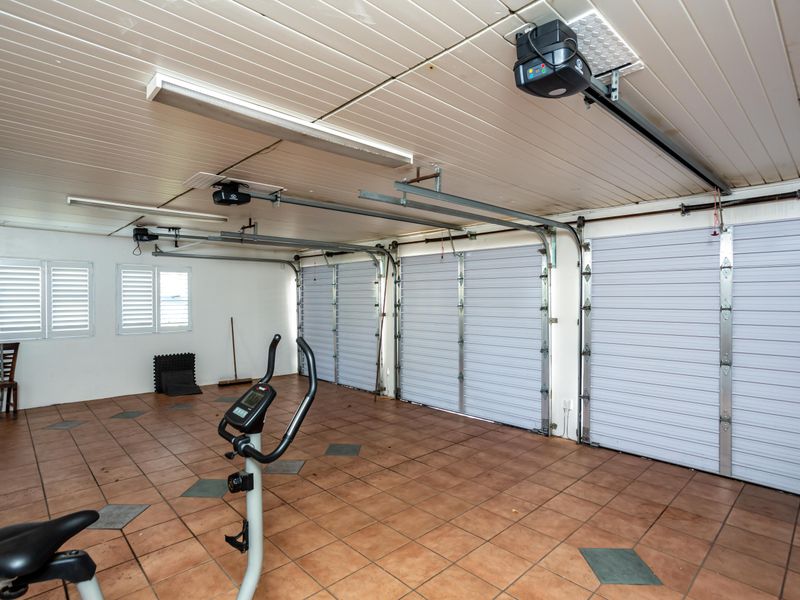 Spacious three-car garage featuring tiled flooring, automatic doors, and functional lighting, providing ample secure parking and storage space.