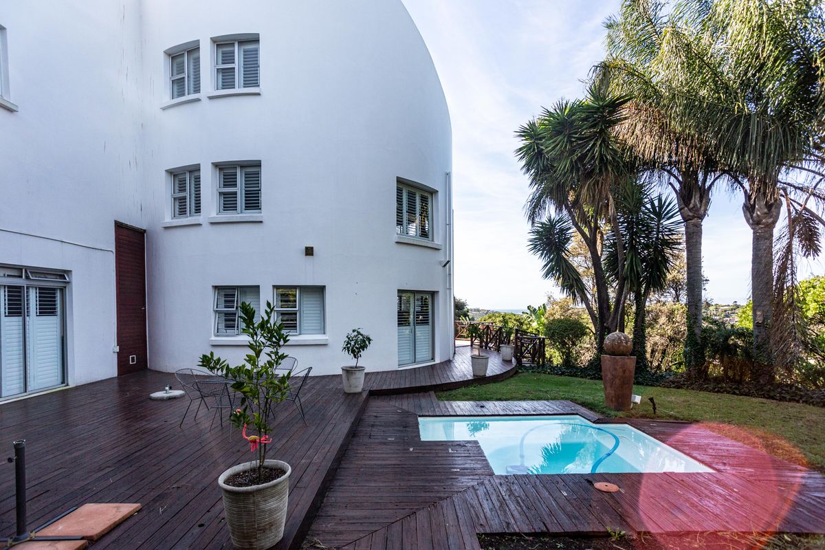 Rear exterior view featuring a curved white building facade, extensive timber decking, and a small swimming pool set within a landscaped garden area.