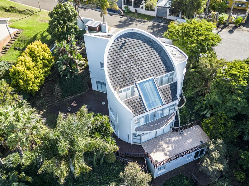 Aerial view of a unique architectural home featuring a distinctive curved roof, integrated skylight, expansive timber decking, and established surrounding gardens.
