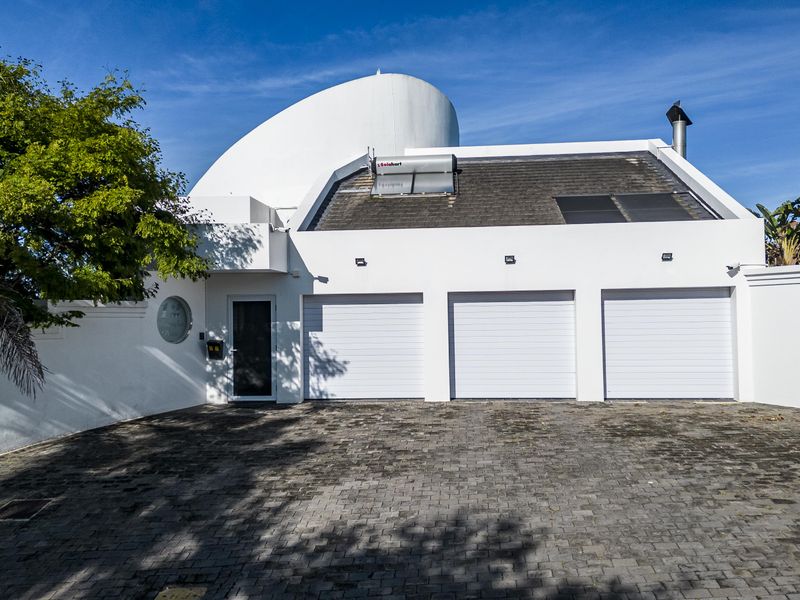 Front elevation of a modern home featuring a triple garage, paved driveway, solar water heating system, and a distinctive architectural dome roof structure.