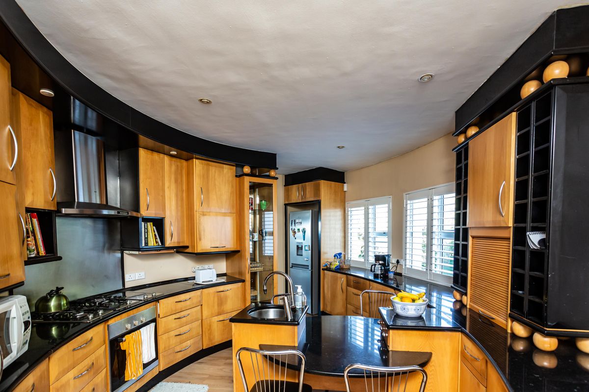 A spacious kitchen featuring warm wood cabinetry, contrasting black granite countertops, integrated appliances, and plantation shutters, offering a functional and well-lit culinary space.