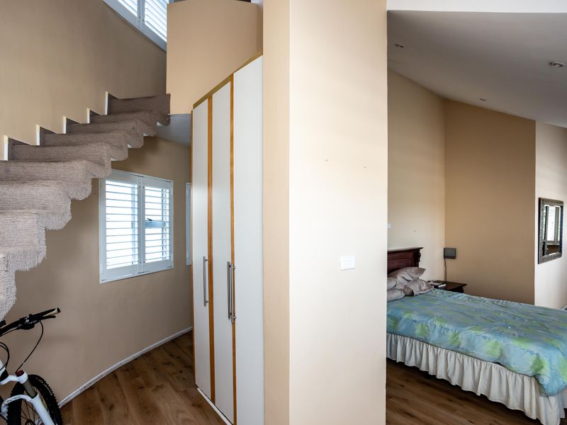 Spacious bedroom featuring built-in wardrobes, laminate flooring, and a unique internal staircase leading to an upper level, complemented by plantation shutters.