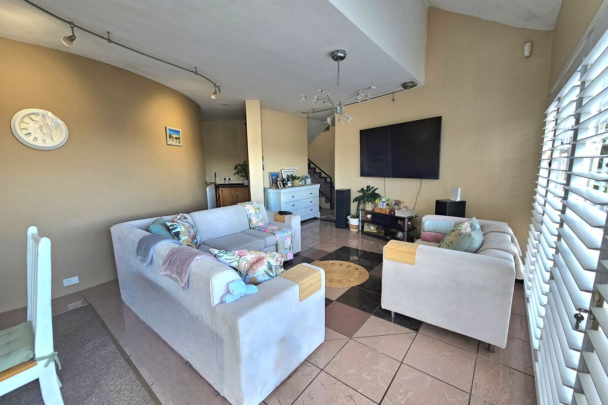 Spacious living room featuring tiled flooring, track lighting, and shutter blinds, with an open-plan layout leading to the staircase area.