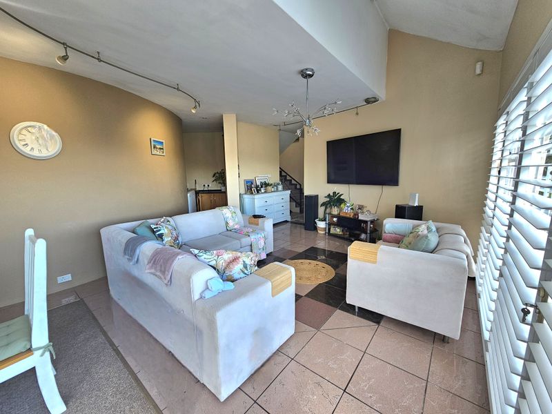 Spacious living room featuring tiled flooring, track lighting, and shutter blinds, with an open-plan layout leading to the staircase area.