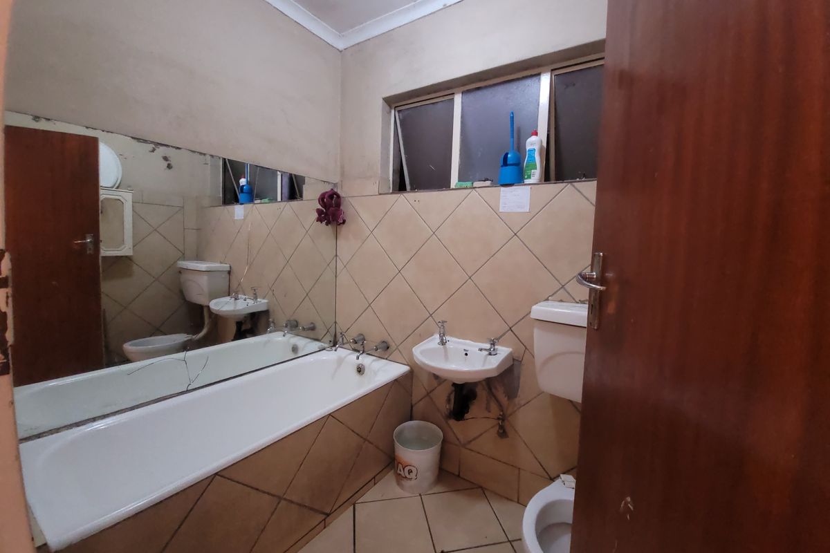A dated bathroom featuring a bathtub, wall-mounted basin, and toilet, with tiled finishes and a large wall mirror requiring maintenance and cosmetic updates.