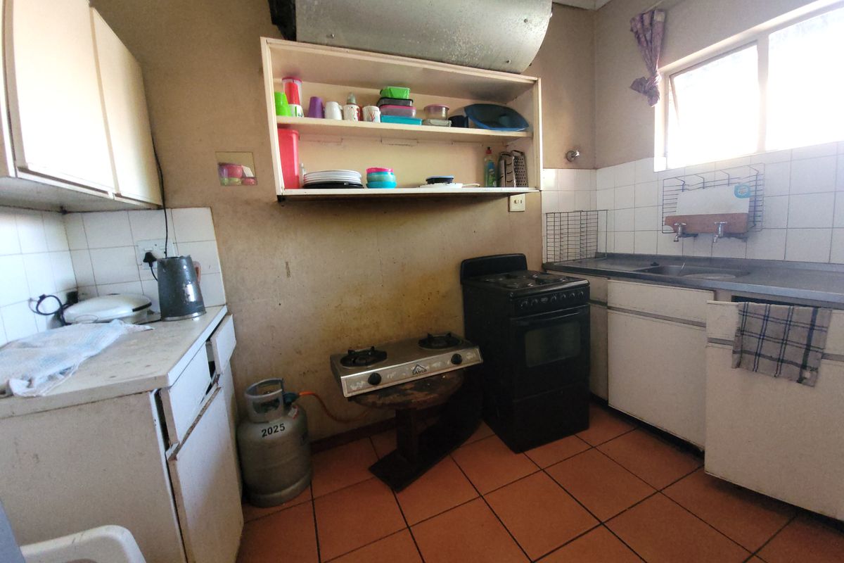 A dated kitchen featuring tiled flooring, built-in cabinetry, a stainless steel sink, and both electric and gas cooking appliances.