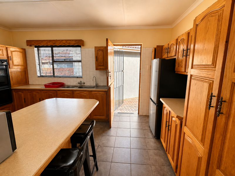 A functional kitchen featuring traditional wooden cabinetry, laminate countertops, tiled flooring, and direct access to an outdoor area through a security door.