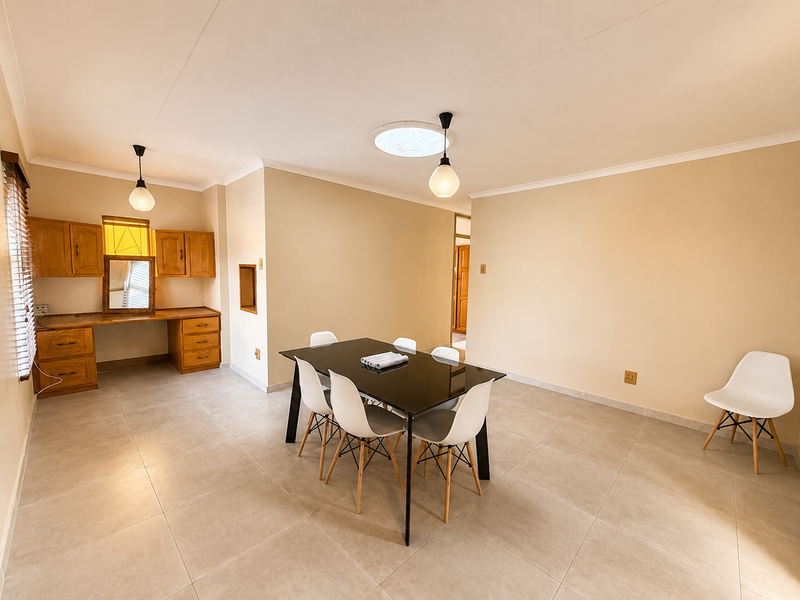 Spacious dining area featuring neutral tiled flooring, a built-in wooden desk with cabinetry, a central skylight, and modern pendant lighting.