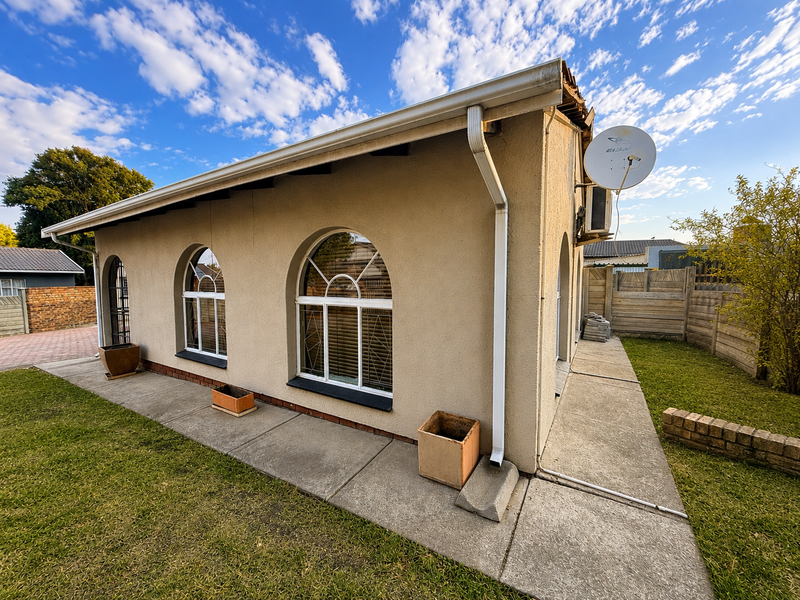 Rear exterior view of the house featuring arched windows, a concrete patio, and a small garden area with a brick retaining wall.