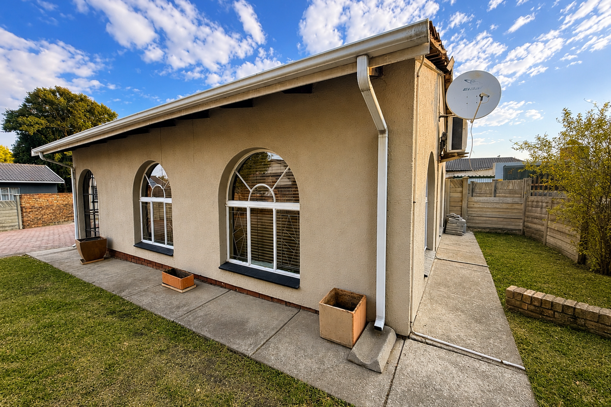 Rear exterior view of the house featuring arched windows, a concrete patio, and a small garden area with a brick retaining wall.