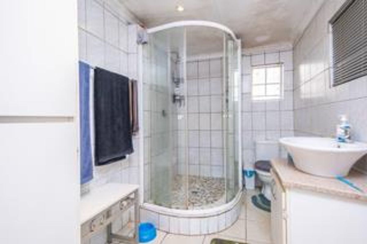 Functional bathroom featuring a corner shower enclosure, vanity basin, toilet, and tiled finishes throughout.