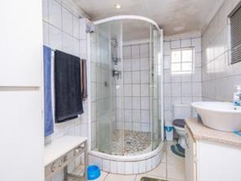 Functional bathroom featuring a corner shower enclosure, vanity basin, toilet, and tiled finishes throughout.