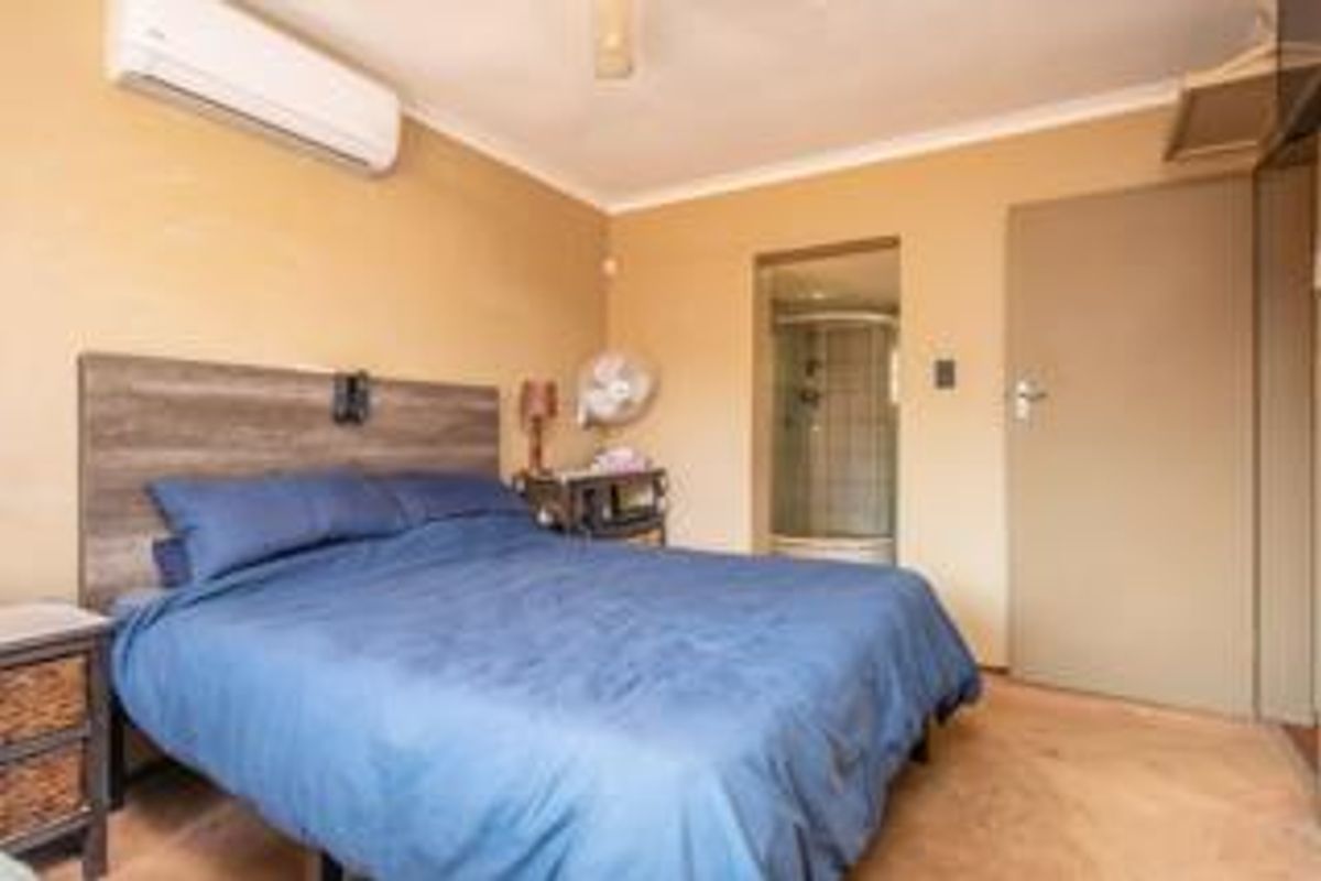 A bedroom featuring tiled flooring, a split-system air conditioner, and an attached en-suite bathroom with a shower enclosure.