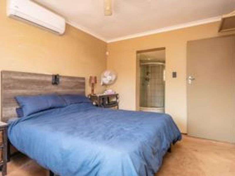A bedroom featuring tiled flooring, a split-system air conditioner, and an attached en-suite bathroom with a shower enclosure.