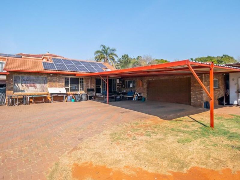 Front exterior view of the house featuring a large paved driveway, a covered carport, and roof-mounted solar panels.