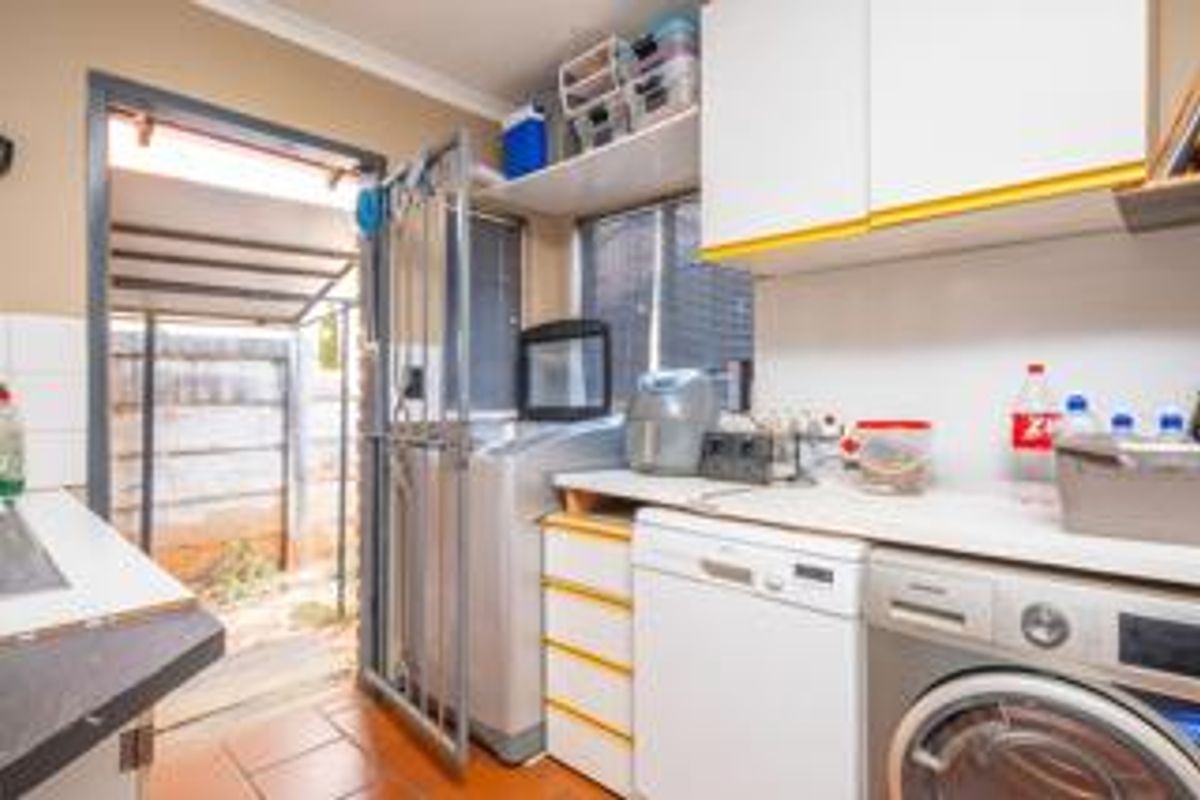 Functional laundry area featuring built-in cabinetry, laminate countertops, and direct access to the exterior through a security gate.