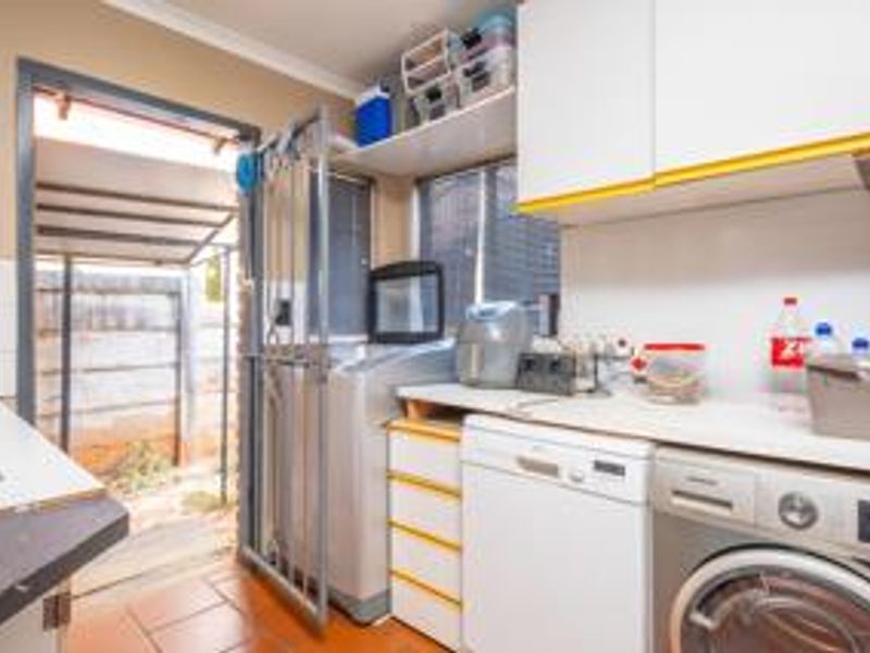 Functional laundry area featuring built-in cabinetry, laminate countertops, and direct access to the exterior through a security gate.