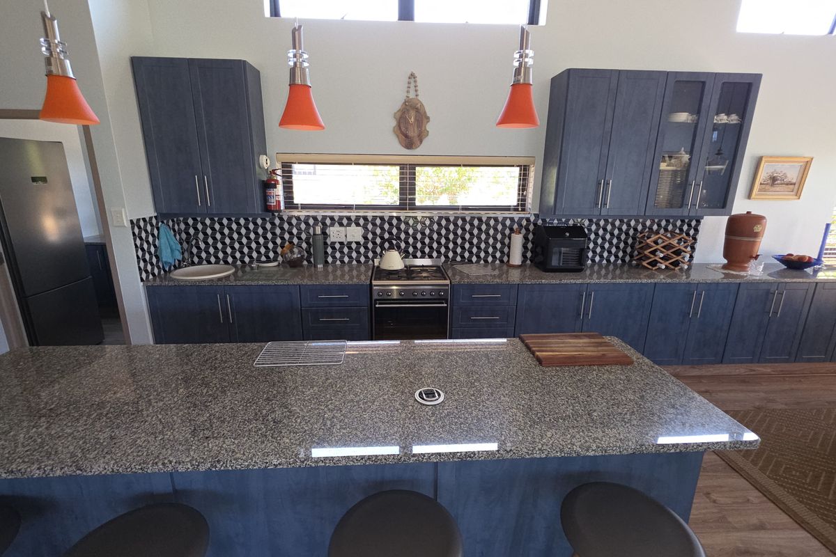 Modern kitchen featuring dark blue cabinetry, granite countertops, a central island with seating, and a geometric tiled backsplash.