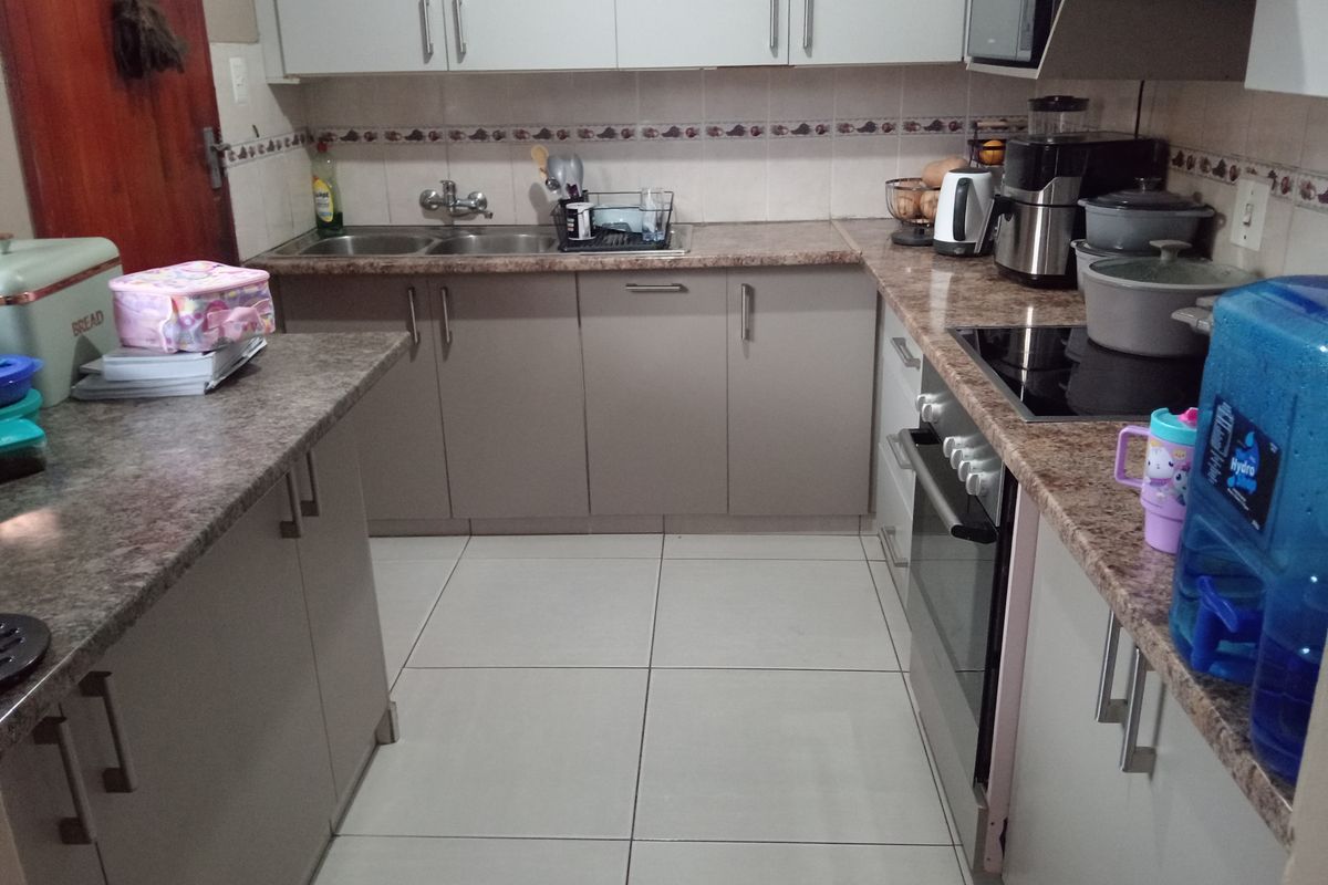 A functional kitchen featuring laminate countertops, built-in oven with electric hob, extractor fan, and ample upper and lower cabinetry with tiled flooring.