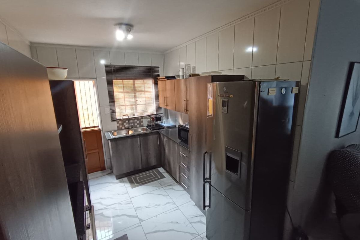 A functional kitchen featuring built-in cabinetry, tiled backsplash, and modern floor tiles, providing a practical workspace with direct access to the exterior.