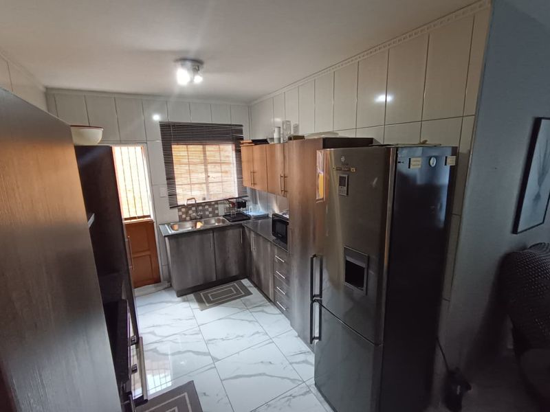A functional kitchen featuring built-in cabinetry, tiled backsplash, and modern floor tiles, providing a practical workspace with direct access to the exterior.