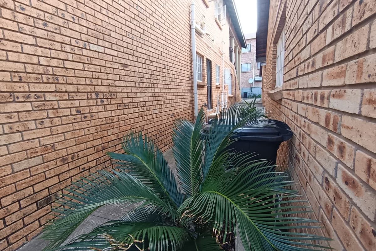 A narrow side passage between two brick townhouse structures featuring concrete paving and exterior drainage infrastructure.