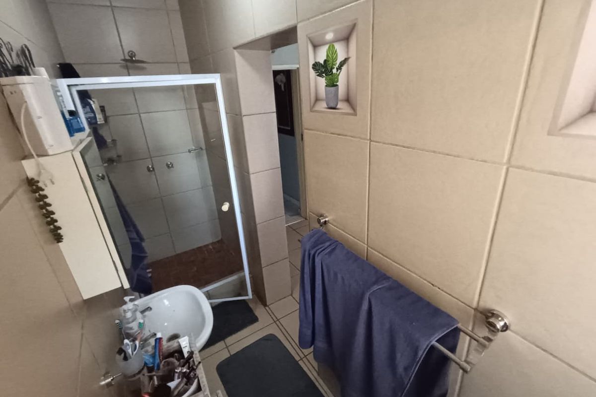 A functional bathroom featuring a shower enclosure, wall-mounted basin, and neutral ceramic wall tiling.