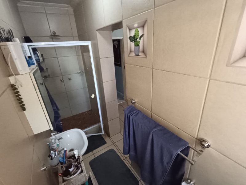 A functional bathroom featuring a shower enclosure, wall-mounted basin, and neutral ceramic wall tiling.
