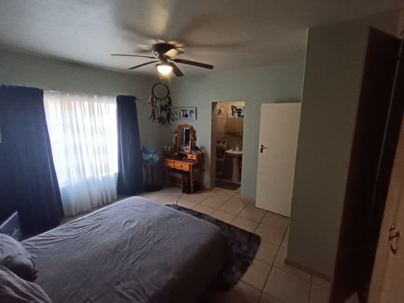 A bedroom featuring tiled flooring, a ceiling fan, and direct access to an en-suite bathroom.
